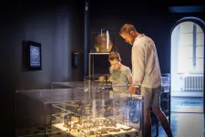 I ett mörkt rum står en liten pojke och hans pappa och blickar ned över en upplyst väggmonter fylld av arkeologiska föremål