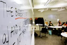 Detaljbild av en whiteboard, med studenter sittande runt bord i bakgrunden. På tavlan står det "the bigger picture". Foto.