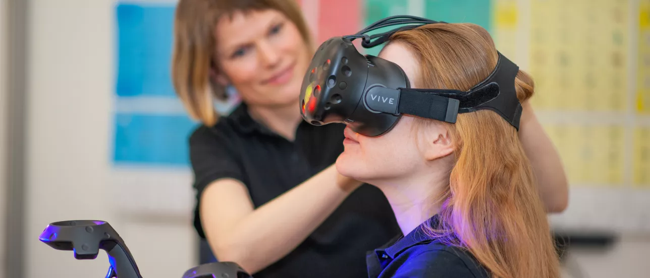 Kvinna med ett par VR-glasögon, får hjälp av annan kvinna. Arbetsterapi vid Lunds universitet.