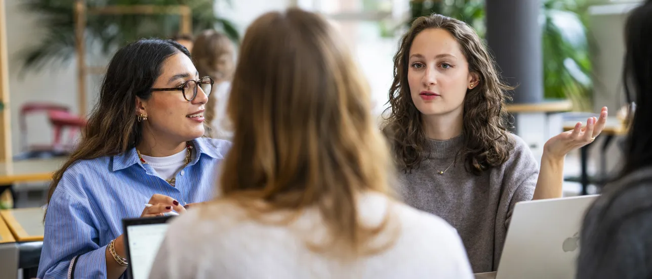 Studenter i diskussion kring ett bord med laptops. Foto