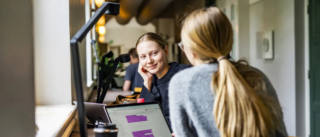 Två studenter sitter och pratar i en korridor.