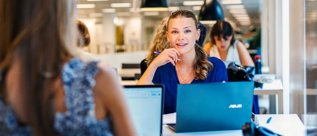 En student sitter vid en dator och tittar in i kameran.