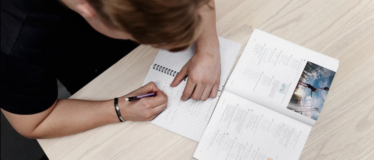 Student som pluggar matte vid ett bord. Foto.