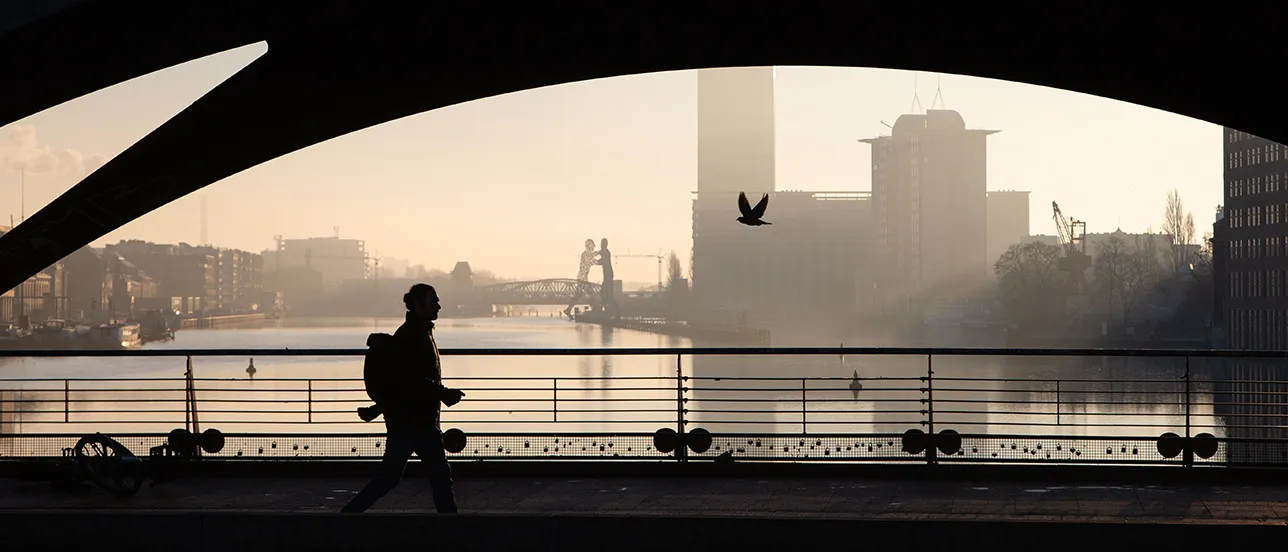 Person går över en bro med vatten i bakgrunden