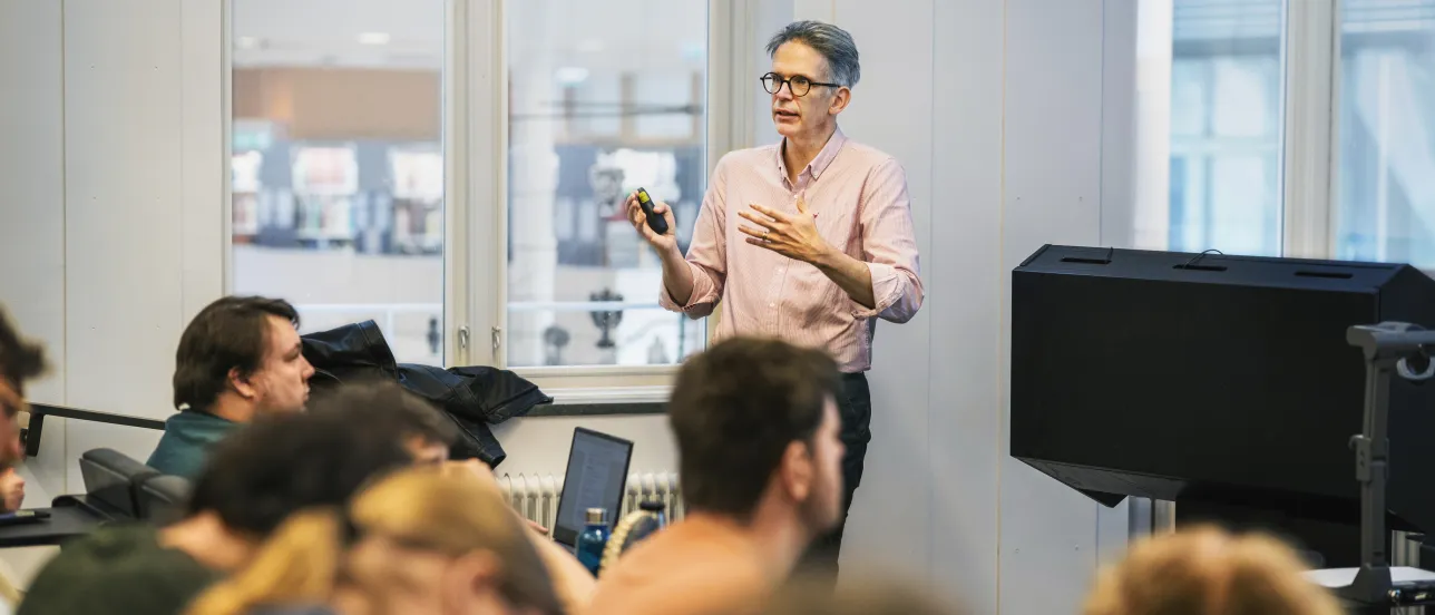 Lärare föreläser för studenter i en ljus föreläsningssal.