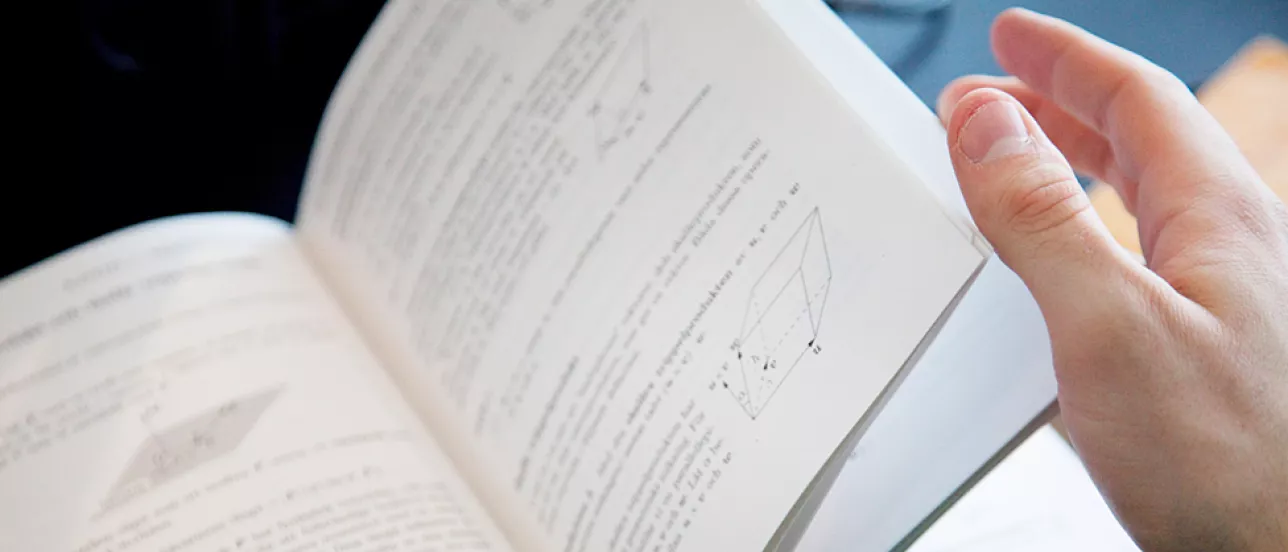En person bläddrar i en bok med formler i. Foto.