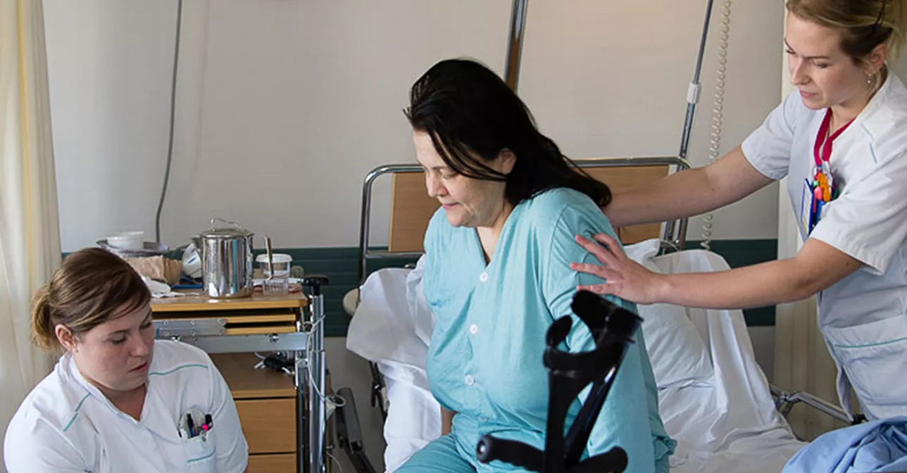Nyopererad patient får hjälp av vårdpersonal. Foto.