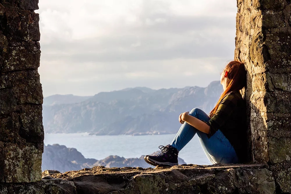 Student i ruin ser ut över fjord i solnedgång. Foto Tim Strulik, Unsplash