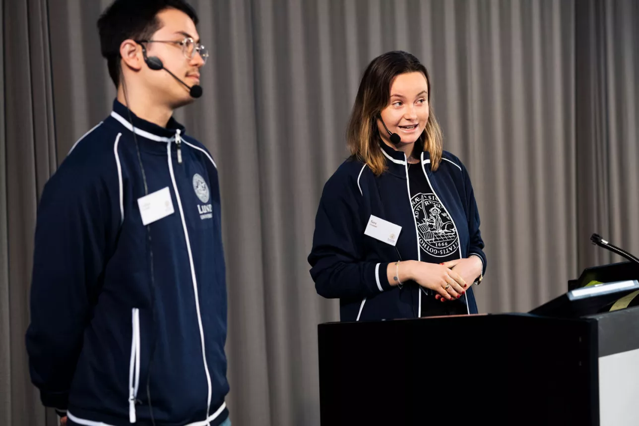 Två studenter står vid ett podium och berättar om sitt liv som Lundastudenter under Öppet hus. Foto: Johan Persson.