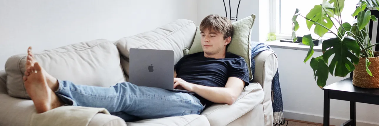 Kille ligger i soffan och pluggar med laptop. Foto.