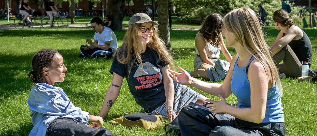 Tre glada studenter sitter i gröngräset. Foto.