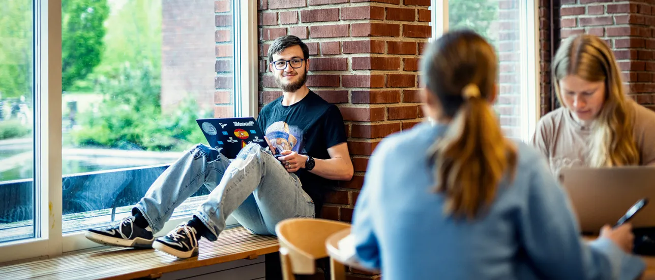 Glad student sitter i fönsterkarm. Foto.