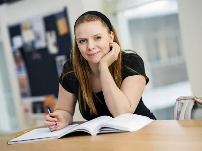 Kvinnlig student som sitter vid ett skrivbord med en öppen bok framför sig. Foto.