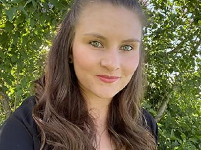 Kvinna som står med gröna blad runt sig och tittar in i kameran. Foto.