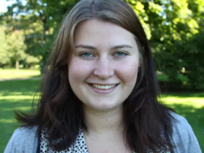 Kvinna som står utomhus med grön bakgrund och tittar in i kameran. Foto.