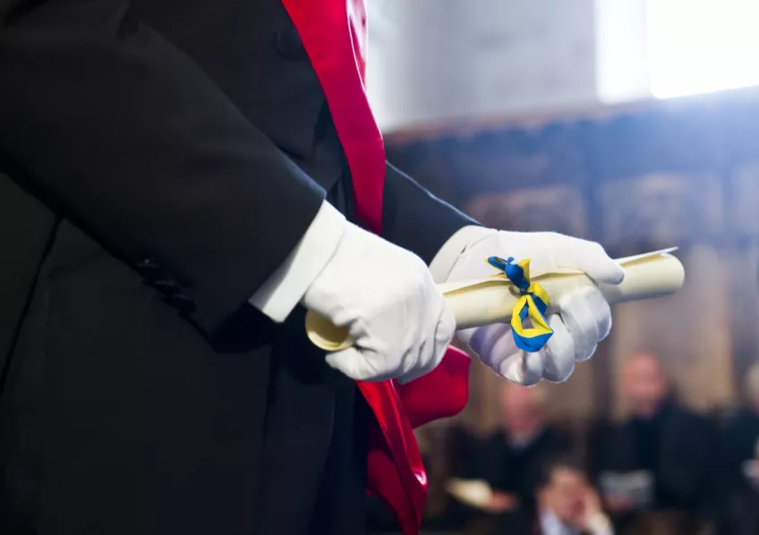 Närbild på ett doktorsdiplom i händerna på en marskalk. Foto.