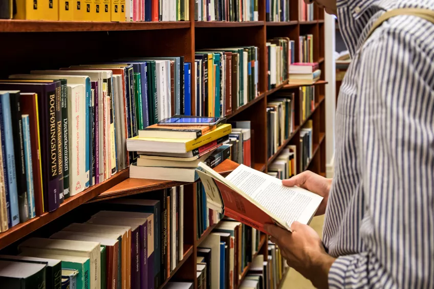 Student iklädd en randig skjorta bläddrar i en bok i Juridiska fakultetens bibliotek.