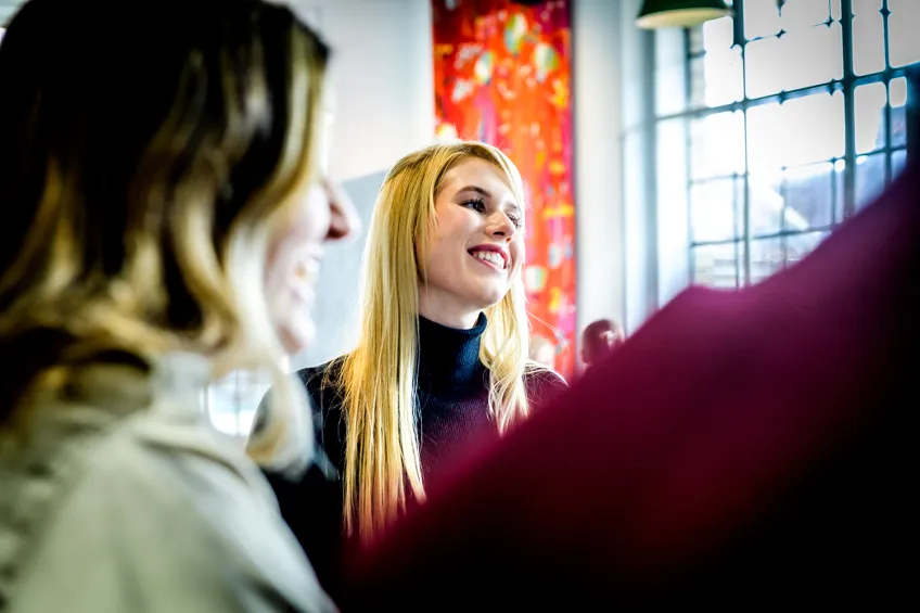 Leende studenter. I bakgrunden ett stort fönster och färgglad gardin.