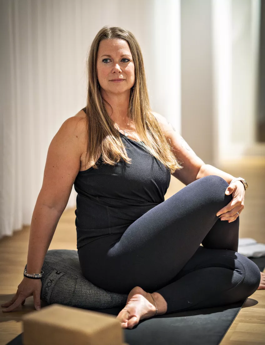 Foto på Maja Petersson som sitter i en yogaposition på golvet inne i Gerdahallens yogastudio.