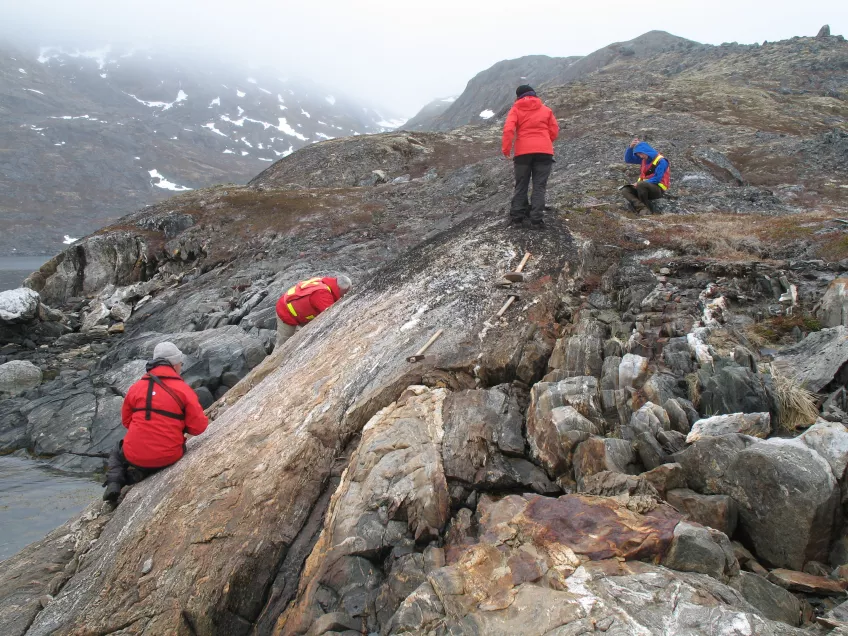 Bild på geologiforskare som klättrar på stenhällar på Grönland.