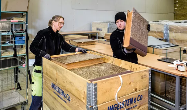 Två personer i arbetskläder packar ner gamla jätteböcker i packlår