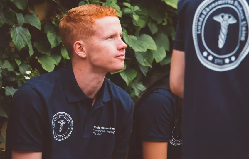 Foto på Tobias utomhus vid en lövbeklädd vägg.